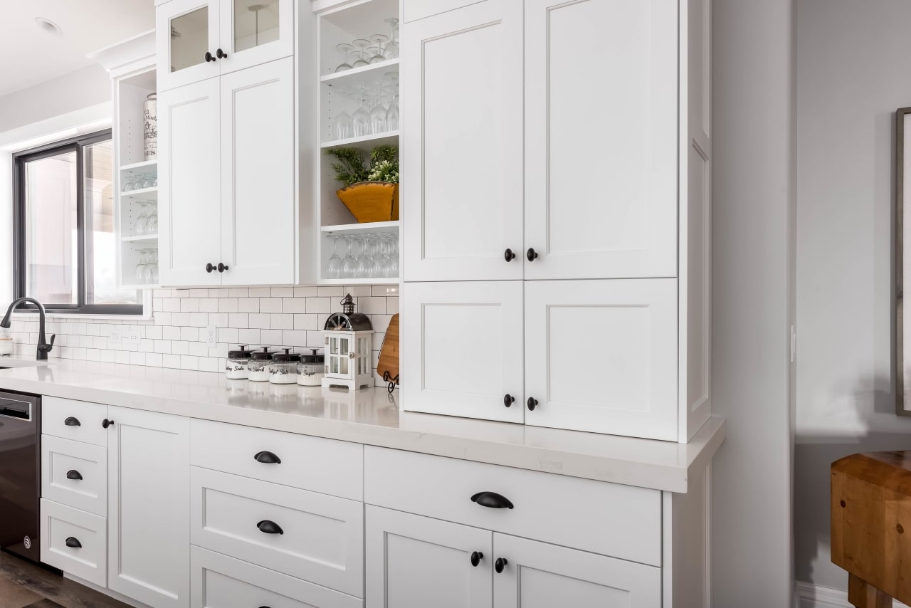 White colored custom cabinets installed on a wall in a kitchen with white tile backsplash.